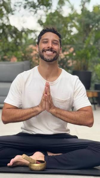 Caio Reis sentado em postura de meditação, com as mãos em prece
